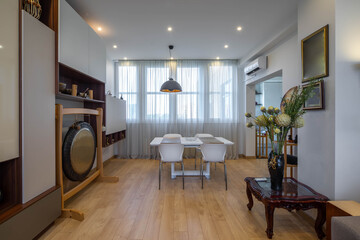 Contemporary interior of luxury flat. Table and chairs in living room. Home decor in asian style. White walls.