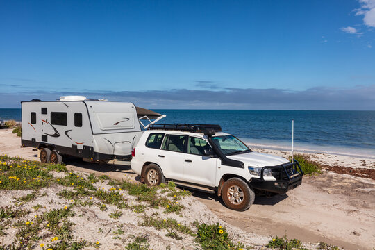 Landscape view of 4WD and modern caravan parked adjacent to a sparkling sunny beach.