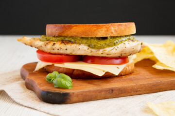 Homemade Pesto Chicken Sandwich with Potato Chips on a rustic wooden board, side view. Close-up.