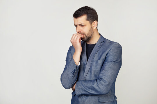 Young businessman with a smile, a man with a beard in a jacket, looks tense and nervous with hands on his lips, biting his nails. Anxiety problem. Portrait of a man on a gray background