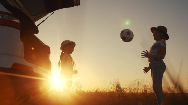 children in the park silhouette playing ball on vacation next to the car. happy family camping kid dreams concept. two sisters fun kids throw a ball each other play silhouette. girl kid on vacation