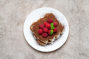 portion of Classic tiramisu dessert with raspberries on grey concrete background