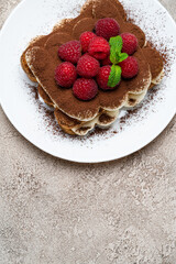 portion of Classic tiramisu dessert with raspberries on grey concrete background
