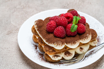 portion of Classic tiramisu dessert with raspberries on grey concrete background