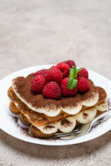portion of Classic tiramisu dessert with raspberries on grey concrete background