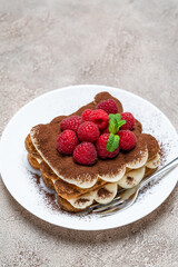 portion of Classic tiramisu dessert with raspberries on grey concrete background
