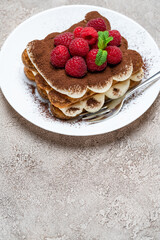 portion of Classic tiramisu dessert with raspberries on grey concrete background