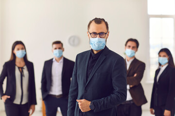 Young company leader with group of responsible workers wear face masks in their workplace