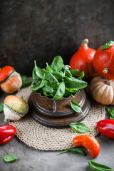 Spinach leaves in a vintage plate on wooden coasters on a dark table. Still life with autumn bright vegetables.