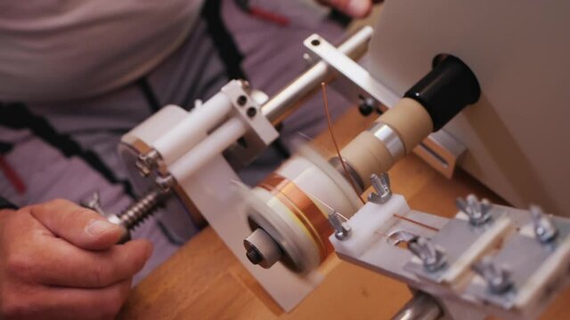 Hands operate coil winding machine, making a transformer component - reeling conducting wire on plastic support, close up, slow motion, top view