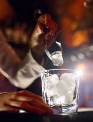 The bartender pours ice into cocktail glasses.