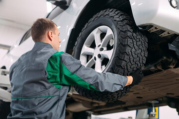 Fototapeta na wymiar Car lifted in automobile service for fixing, worker repairs the wheel,