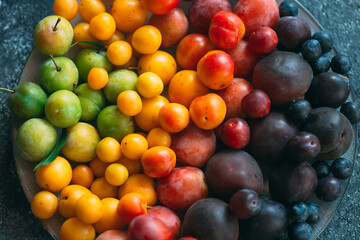 Multicolored plums on a plate are laid out by color.