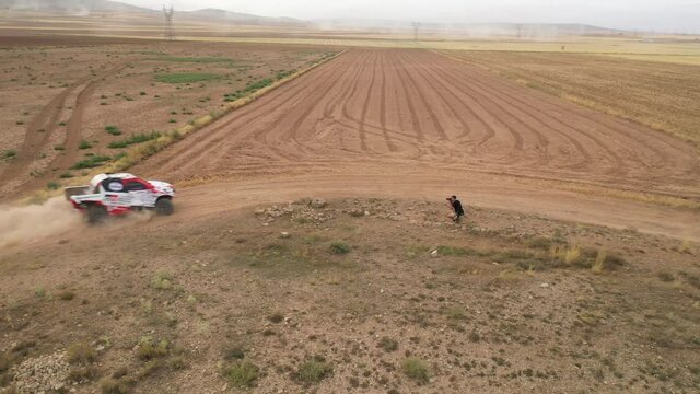 Aerila view of photographer taking pictures of SUV racing car passing the corner at Dakar Rally