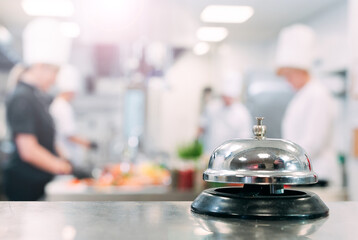 Table distribution in the restaurant. Cooks prepare food in the kitchen against the background of a metal bell.