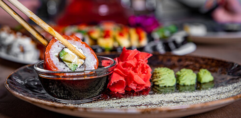 Dipping tasty sushi roll into bowl with soy sauce