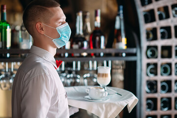 A European-looking waiter in a medical mask serves Latte coffee.