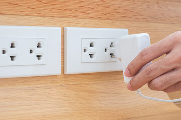 Closeup Male finger unplugging or plugging of electricity device on white wall at home. Energy...