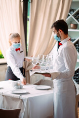 A waiter in a medical protective mask serves a table in the restaurant. Employees of a restaurant or hotel in protective masks. The End Of Quarantine.