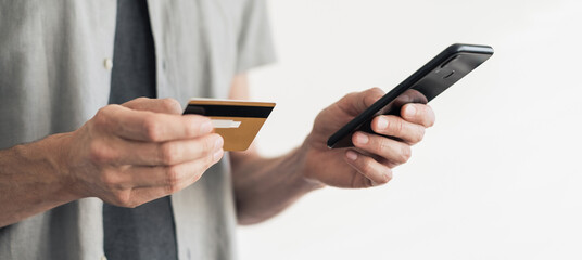 Close-up of man hands holding credit card and using smartphone isolated panoramic banner,...