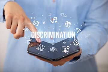 Businessman holding a foldable smartphone with DISCRIMINATION inscription, social media concept