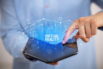 Businessman holding a foldable smartphone with VIRTUAL REALITY inscription, new technology concept