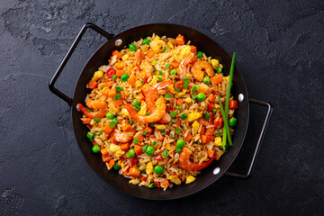 Stir fry rice with vegetables and shrimps in black iron pan. Slate background. Close up. Top view.