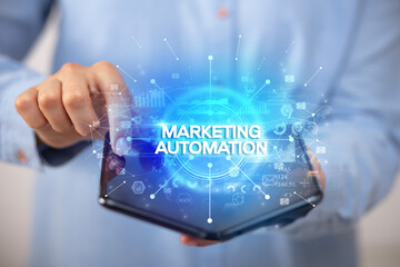 Businessman holding a foldable smartphone with MARKETING AUTOMATION inscription, new business concept