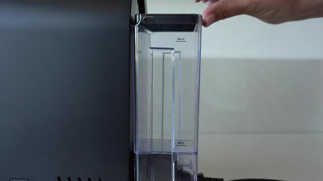 Closeup view video of female hand opens cap of container for fresh water. Woman going to pour some filtered water into small black coffee machine.
