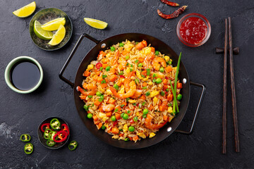 Stir fry rice with vegetables and shrimps in black iron pan. Slate background. Close up. Top view.