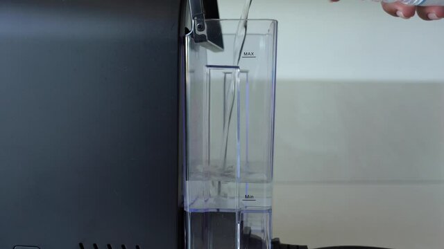 Closeup view 4k video of female hand adding fresh filtered water into small black coffee machine.
