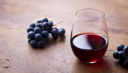 Glass of red wine with fresh grape on wooden table. Copy space.
