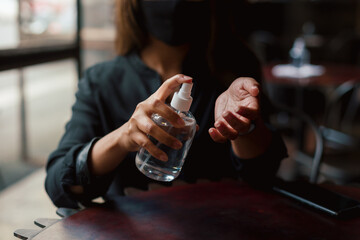 Young woman sanitising hands with pray bottle in cafe