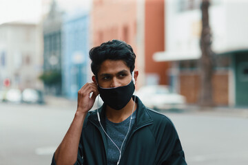 Young Indian man listening to music on earphones with facemask