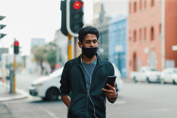 Young man looking at phone while walking on street with facemask