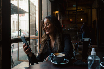 Young woman laughing at phone in dark cafe