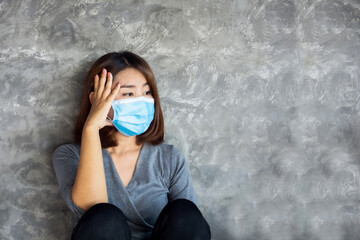 depressed Asian woman wearing  face mask sitting alone next to the wall 