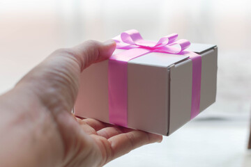 hands holding a gift with white box and pink ribbon