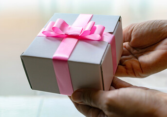 hands holding a gift with white box and pink ribbon