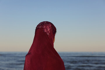 woman with purple veil on her head by the sea awaits the arrival