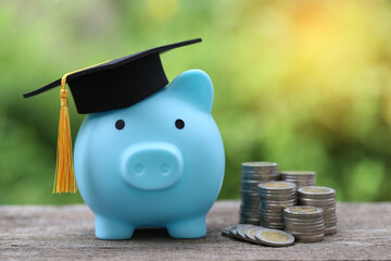 Graduation hat on blue piggy bank with stack of coins money on nature green background, Saving money for education concept