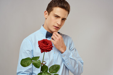 Handsome man with red rose blue shirt bow tie light background cropped view