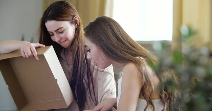 Couple Of Girls Sitting Together On Couch. Women Bought Blouse From Online Store, Received Package, Opened Box With Delivered Gift, Took Out Clothes, Fighting Over Jacket, Could Not Share Clothes.