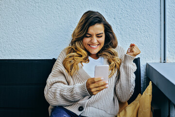 Young excited woman reacting  to news on phone, holding fist celebrating success, having great time
