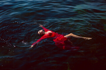 woman swims in the sea in a red long dress with sunglasses