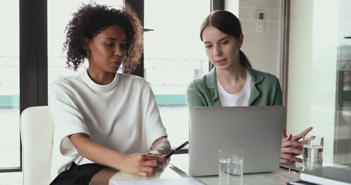 Young african american leader presenting online project to motivated female intern at meeting. Two multiracial businesswomen discussing corporate software at brainstorming meeting in office.