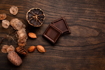 Composition of chocolate two pieces on a wooden background, dried lemon, raisins, plums, pears, walnuts and seeds of chocolate pieces. Conceptual background with chocolate to advertise tea, coffee