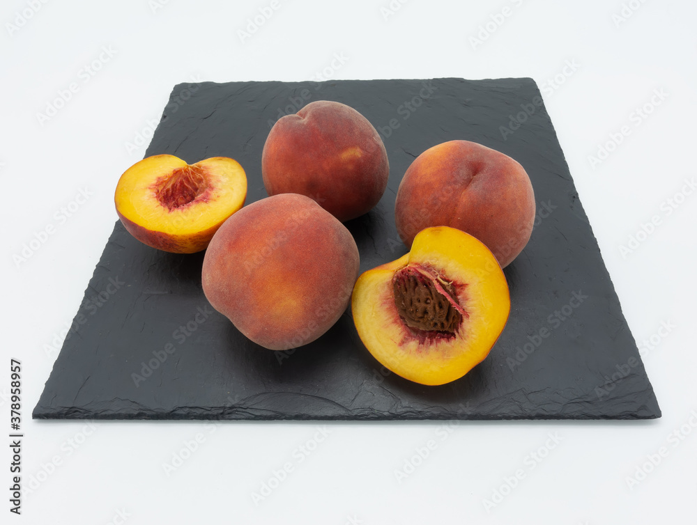 Wall mural ripe peaches on a black square plate. three whole fruits and two halves. white background.