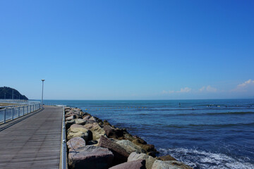 Blue sky and sea, pier. People surfing on sea waves. Beach next to Enoshima Island, Japan