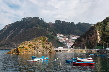 Fishing boats at the sea. Calm water at the natural harbor between cliffs. Small fishing village with white houses built on the hill. Cudillero, Asturias, North of Spain